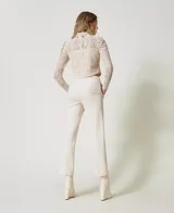 Pantalón de vestir color crema, de corte recto y tiro alto, confeccionado en tejido de punto milano con mezcla de viscosa elástica. Presenta bolsillos laterales inclinados, raya permanente y tira en la cintura con hebilla metálica con logo de la marca. Cierre lateral con cremallera.