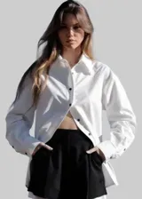 Camisa blanca de corte asimétrico con cierre lateral, cuello clásico y mangas largas con puños abotonados.
