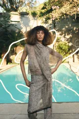 Falda pantalón de tiro bajo con estampado de puntos negros sobre fondo beige. Presenta un diseño de superposición con cierre lateral mediante lazadas y cremallera oculta, finalizando en bordes con detalle de franja negra.