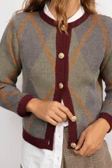 Cardigan de punto con patrón argyle en tonos azul marino, celeste y naranja. Presenta cuello redondo, cierre frontal con botones dorados y terminaciones en tejido acanalado gris.
