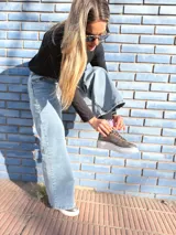 Zapatillas deportivas de cuero color peltre, con cordones negros y suela de goma blanca.