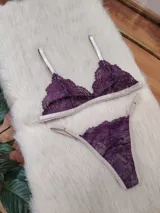 Conjunto de lencería compuesto por un bralette triangular y una bombacha tipo tanga, confeccionados en encaje color violeta con terminaciones y breteles en color tostado.