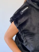 Chaleco de peluche negro con cuello alto, cierre frontal, bolsillos delanteros y detalles decorativos en los hombros.