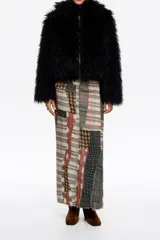 Chaqueta de pelo sintético negro con textura de pelo largo, cierre frontal con cremallera y cuello alto. Diseño de corte corto y envolvente.