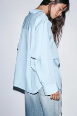 Camisa de corte oversize con estampado de rayas verticales en tonos celeste y blanco. Presenta cuello solapa, escote en pico, manga larga con puños abotonados y un bolsillo de plastrón en el pecho.