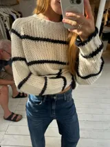 Buzo de tejido de punto grueso en color gris con rayas horizontales en color crema, de corte holgado, cuello redondo y mangas largas.