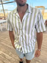 Camisa de manga corta con cuello cubano, confeccionada en tejido de algodón con diseño de rayas verticales en color verde y blanco. Presenta cierre frontal con botones de madera.
