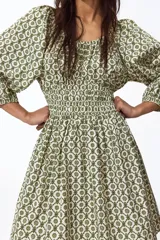 Vestido corto de algodón con estampado geométrico en tonos verdes y blancos. Cuenta con escote en V, mangas globo con elástico en los puños, cuerpo fruncido tipo nido de abeja en la cintura y falda con vuelo.
