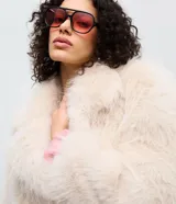 Saco corto de pelo artificial en color beige, con cuello amplio, mangas largas y diseño holgado. Cuenta con forro interior de poliéster.