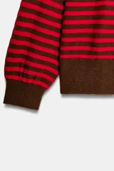 Jersey de punto con diseño a rayas horizontales en color rojo y marrón. Presenta cuello redondo, manga larga con puños ajustados y ruedo acanalado.