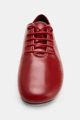 Zapato plano de piel color rojo, con cierre de cordones al tono, puntera redonda y suela baja.