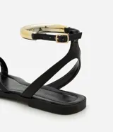 Sandalias planas negras con tira fina en el dedo y pulsera al tobillo con hebilla y aplique dorado.