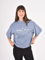 Remera de corte holgado y diseño oversize, color gris azulado con efecto lavado. Presenta un estampado gráfico central con tipografía y motivos florales.