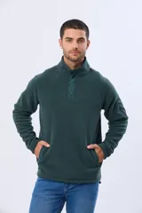 Buzo de abrigo confeccionado en tejido polar térmico, diseñado para mantener el calor y ofrecer resistencia al viento. Presenta un cuello alto con cierre frontal de broches, bolsillos laterales con cierre y un bolsillo adicional con cierre en la manga izquierda.