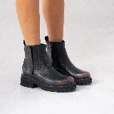 Bota corta estilo chelsea de cuero vacuno negro con acabado desgastado en tono marrón en la puntera y laterales. Presenta elástico lateral, cierre interno y suela de goma tipo track con plataforma.