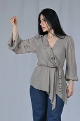 Blusa color gris beige con escote cruzado en V y volados en el frente. Tiene mangas largas con puños elásticos y corte a la cintura con lazo lateral.