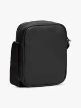 Bandolera reporter Tommy Hilfiger de color negro, confeccionada en poliuretano con acabado liso y panel frontal inferior con detalle tejido. Cuenta con un compartimento principal con cierre de cremallera, bolsillo exterior frontal también con cremallera, bolsillo interior abierto, correa ajustable y logo metálico de la marca en la parte delantera.