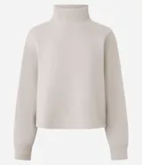 Buzo deportivo de corte boxy, color beige, con cuello alto y puños acanalados. Presenta un diseño minimalista sin estampados, confeccionado en una mezcla de algodón y poliéster.