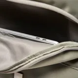 Mochila de diseño minimalista en color verde oliva, confeccionada en material textil suave. Cuenta con un compartimento principal con cierre de doble cremallera, un bolsillo frontal con solapa y cierre de hebilla tipo clip, y un asa superior reforzada.