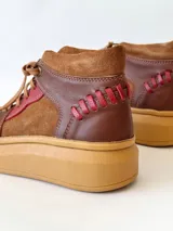 Zapatillas acordonadas de cuero marrón con detalles en rojo y suela de goma color caramelo.