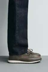 Zapatilla deportiva color verde militar, con parte superior de múltiples piezas que combinan piel y serraje. Presenta horma redonda y suela dentada en color crema con base marrón.