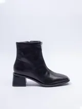 Botín negro de cuero sintético, caña corta, con punta cuadrada y cierre frontal central. Posee un taco bajo y grueso.