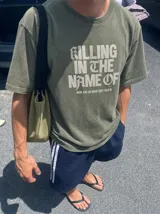 Remera gris con efecto acid wash y diseño oversize. Presenta un estampado frontal con la inscripción "KILLING IN THE NAME OF" y la frase "NOW YOU DO WHAT THEY TOLD YA".