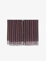 Capa o poncho de tejido de punto con cuello en V y flecos en el borde inferior. Presenta un patrón de rayas verticales en zigzag con una rica paleta de colores que incluye tonos marrones, negros, rojos, naranjas y morados.