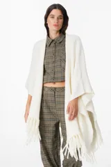 Ruana de tejido suave y envolvente en color blanco, con diseño de corte amplio y terminación de flecos en el ruedo.