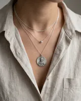Collar triple de plata con cadenas finas de eslabones. El diseño incluye una cadena superior con un pequeño cilindro, una intermedia con una cuenta esférica y una inferior con un dije circular grabado con la imagen del Sagrado Corazón.