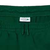Pantalón de jogging verde oscuro con puños elásticos y cintura ajustable con cordón. Presenta bolsillos laterales y logo de Lacoste estampado en blanco en la pierna izquierda.