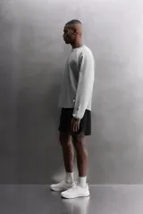 Camiseta de algodón gris de corte relajado con mangas largas ranglán de color gris más claro y puños elásticos. Presenta un pequeño bordado en el pecho y un parche con logo en la parte inferior delantera.