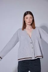 Saco tejido en lambswool con diseño de rombos y trenzas en el frente. Presenta cierre frontal con botones, cuello en V y detalles de rayas en contratono en puños y ruedo. Incluye pin bordado en la manga.