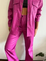 Camisa fucsia de cuero sintético con textura croco, corte recto, cuello camisero, cierre frontal con botones a presión, mangas largas y bolsillos de parche en el pecho.