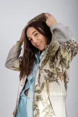 Canguro con capucha y cierre frontal, color beige con estampado de hojas en tonos marrones y amarillos. Mangas largas en color gris.