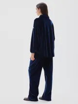 Camisa de terciopelo color negro, con cuello clásico, cierre frontal oculto y mangas largas con puños elásticos. Presenta un diseño holgado con cordón ajustable en el ruedo.