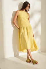 Vestido midi negro sin mangas, con cuello redondo, corte recto en la parte superior y falda amplia con vuelo. Presenta costuras decorativas verticales y un detalle deshilachado en el dobladillo inferior.