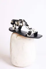 Sandalias planas con diseño de estampado animal print tipo vaca, con puntera cuadrada, tira en T y cierre con hebilla ajustable en el tobillo.