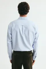 Camisa H&M de algodón Oxford a rayas celestes y blancas, con cuello americano, bolsillo en el pecho y mangas largas.