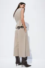 Pantalón sastrero de corte cropped y tiro alto, con piernas amplias y pliegues frontales. Presenta cierre con botón y trabillas en la cintura, en un tono beige con estampado de microcuadros.