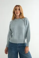Buzo de tejido de punto color celeste, con cuello redondo, mangas largas con costuras raglán y puños y ruedo acanalados.