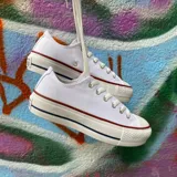 Championes Converse Chuck Taylor All Star de lona blanca con plataforma, cordones blancos y detalles en rojo y azul en la suela.