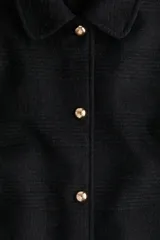 Abrigo de largo hasta la rodilla, confeccionado en mezcla de lana, color negro con textura sutil a cuadros. Presenta un corte evasé, cuello solapa, cierre frontal con botones dorados y bolsillos laterales insertados.