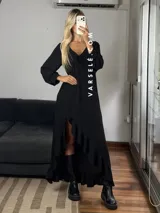 Vestido largo color marrón, con escote en V, mangas largas con puños y detalle de encaje en el pecho. Presenta un diseño asimétrico con volados en el ruedo y una abertura frontal.