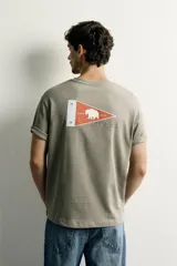 Camiseta verde militar de corte regular, con cuello redondo, manga corta y un bolsillo de parche en el pecho con etiqueta decorativa contrastante.