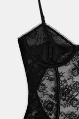 Body de encaje negro con diseño de corsetería, escote en pico y tirantes finos ajustables. Presenta paneles de encaje floral con transparencias y costuras estructuradas.