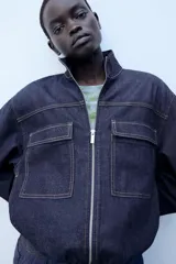 Cazadora bomber de denim oscuro con cuello subido, manga larga y bolsillos frontales con solapa. Presenta cierre frontal de cremallera y bajo elástico.