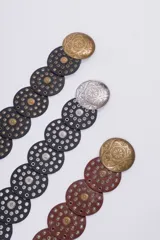 Cinturón de cuero con diseño de discos circulares superpuestos, adornados con tachas y hebillas redondas grabadas. Disponible en negro, marrón y con hebillas en tonos dorado y plateado.