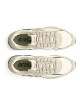 Championes Under Armour Essential Runner de diseño retro, confeccionados con una combinación de nailon ligero y revestimientos de gamuza. Presentan una entresuela de EVA acolchada, plantilla de espuma de lujo y suela de goma completa para mayor tracción. El diseño destaca por su paleta de colores neutros con detalles en verde oscuro en el logo y la entresuela.