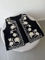 Chaleco marrón con bordados florales en color crema en los bordes y el frente. Presenta un diseño sin mangas con escote en V.